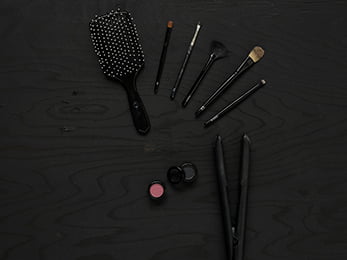 Föremål som representerar Hår- och makeupstylist ligger utlagda på mörkt trä.