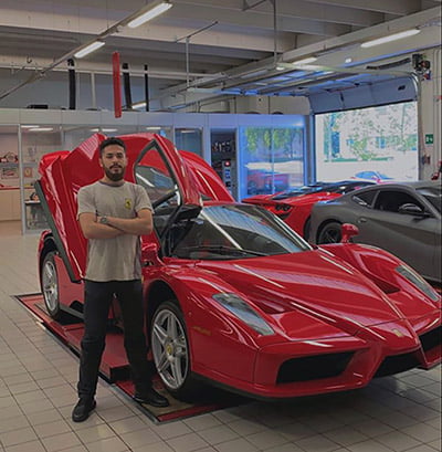 Före detta elev står i ett garage i Italien med en Ferrari bakom sig