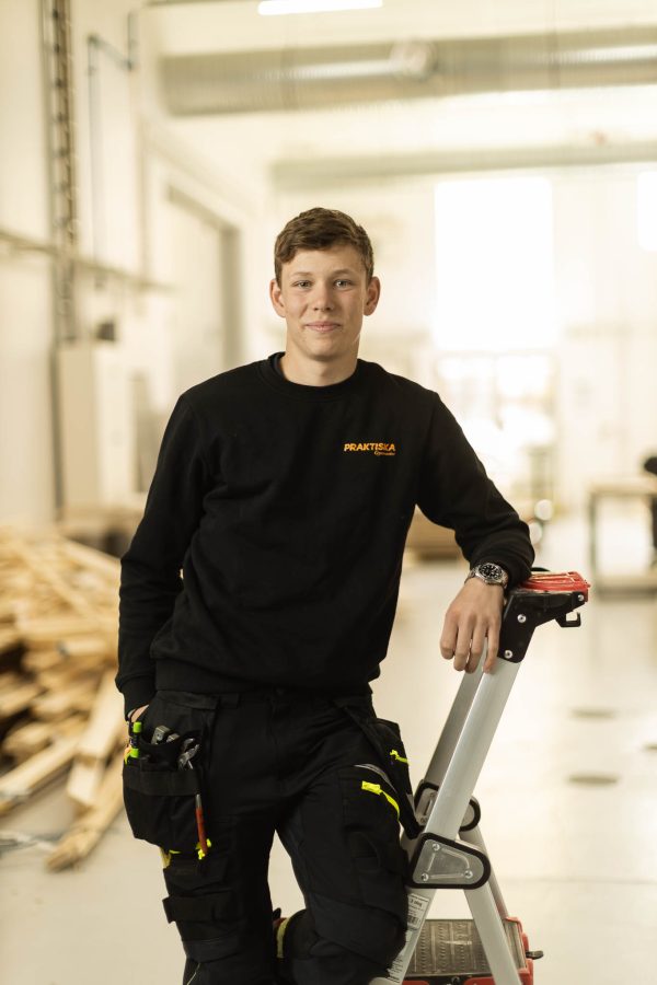Elev i Praktiskatröja står på en stege i en verkstad