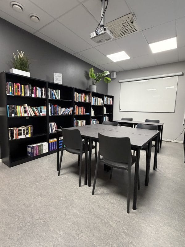 Ett skolbibliotek med en bokhylla samt ett bord med fyra stolar.