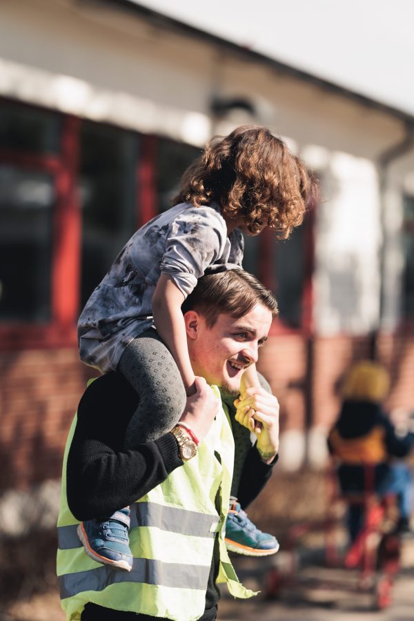 APL-elev från Pedagogiskt och socialt arbete har ett barn på axlarna ute på en skolgård.