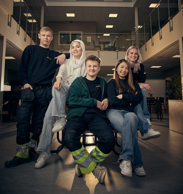 Fem elever som sitter runt ett bord och alla är vända mot kameran.
