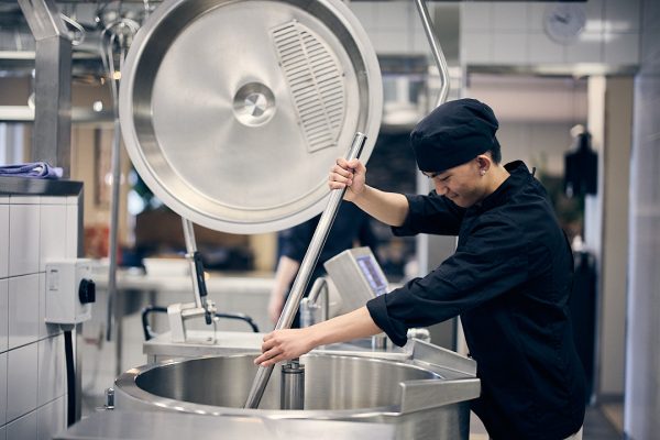 Elev som rör om i en stor gryta i restaurangköket på skolan.