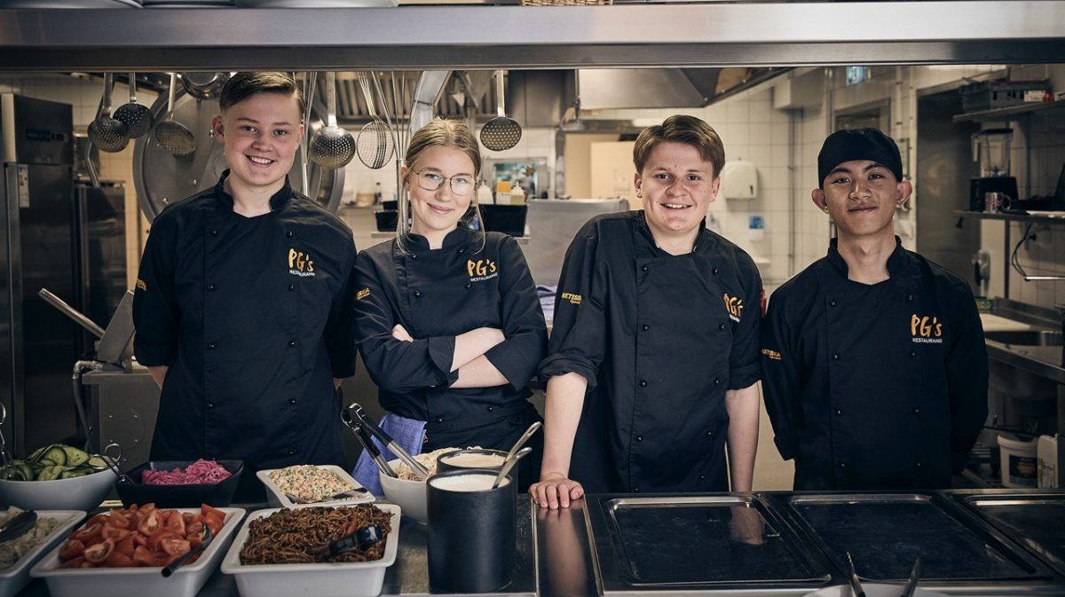 Fyra elever som står i ett restaurangkök och tittar in i kameran