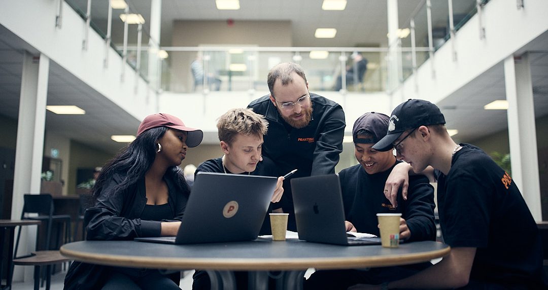 Fyra elever som pluggar i skolan och får hjälp av en lärare.