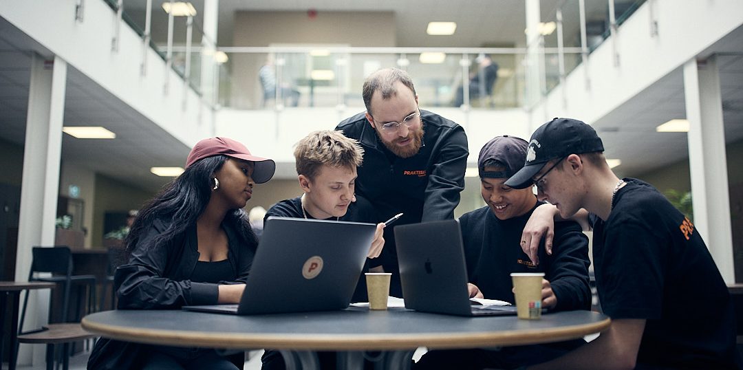 Fyra elever som pluggar runt ett bord i skolan och får hjälp av en lärare.