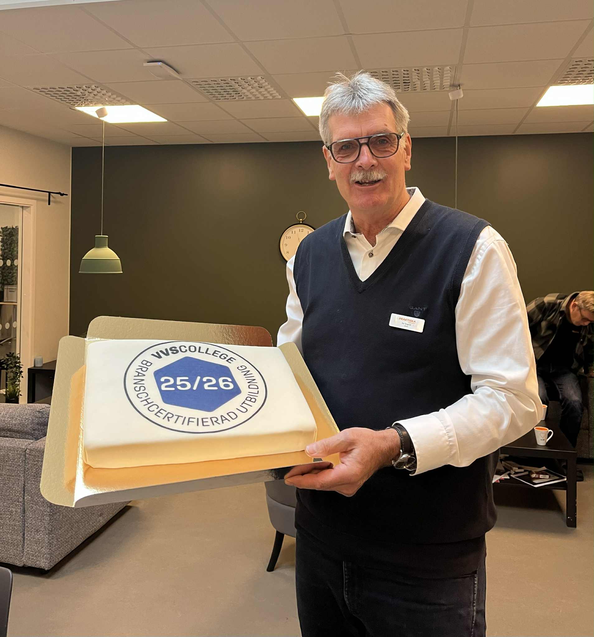 En man som håller i en tårta med texten "VVS college 25/26"