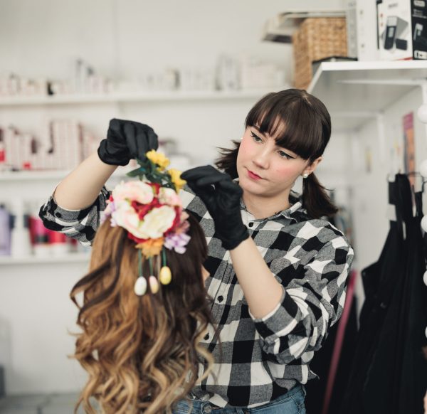 Elev på hår- och makeupstylist sätter blommor i en peruk.